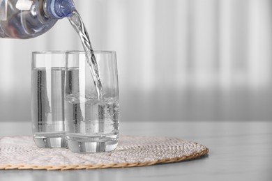 Pouring water from bottle into glass on table against blurred background, space for text