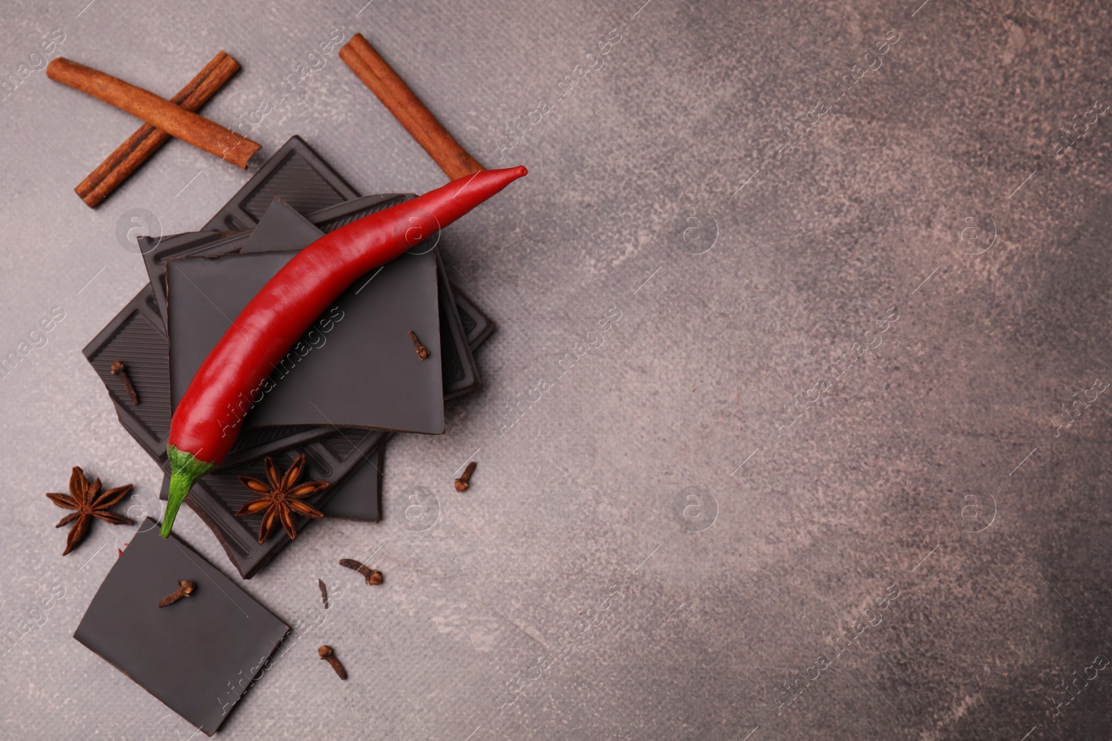 Photo of Delicious chocolate, fresh red chili pepper and spices on grey textured table, flat lay. Space for text