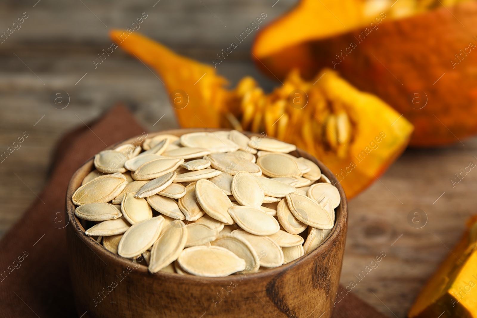 Photo of Bowl of raw unpeeled pumpkin seeds on wooden table, closeup