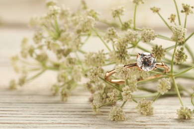 Beautiful engagement ring with gemstone and flowers on white wooden table, closeup. Space for text