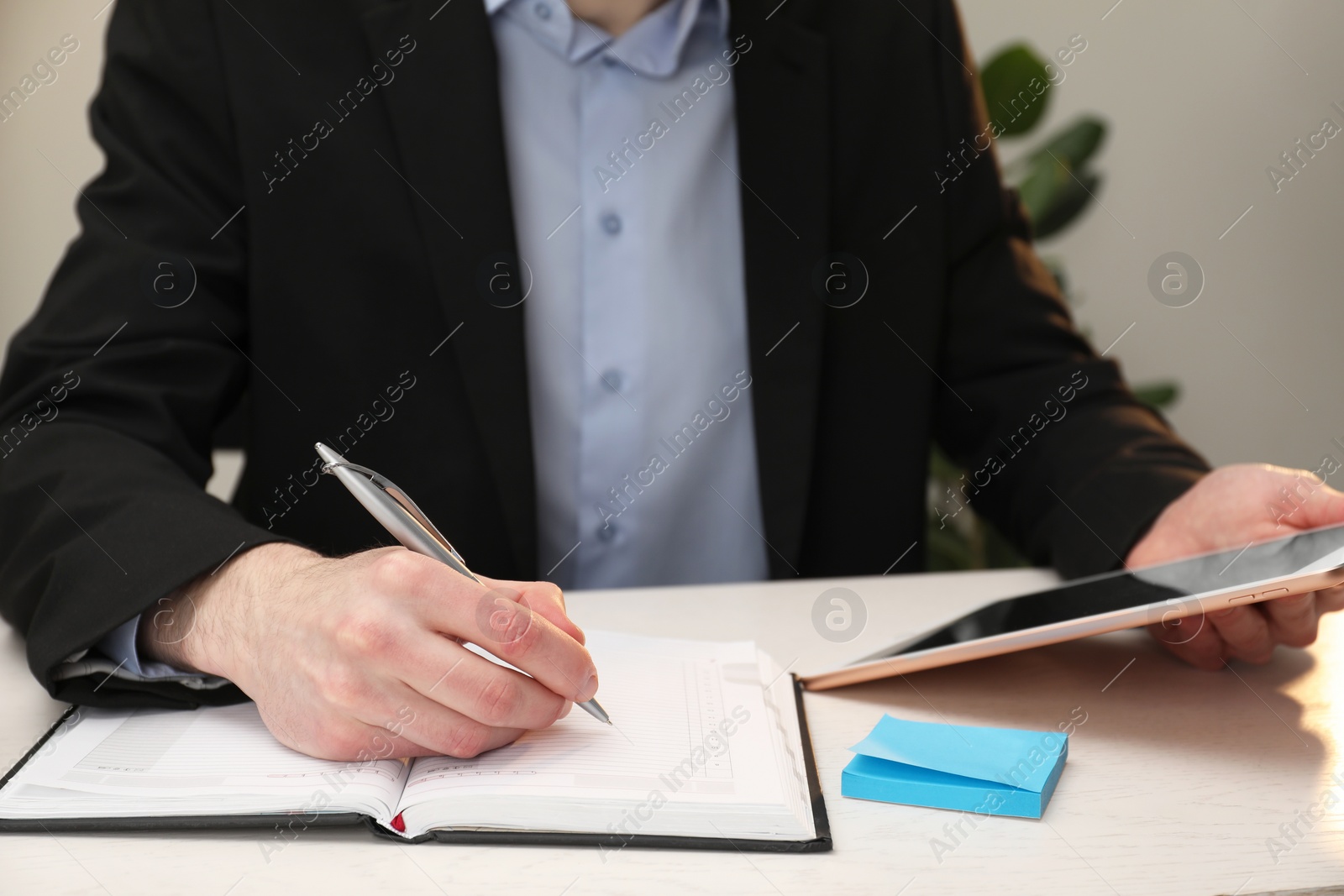 Photo of Man taking notes at white wooden table indoors, closeup