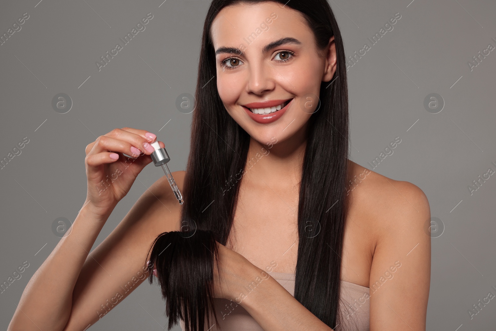 Photo of Beautiful woman applying hair serum on grey background. Cosmetic product