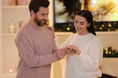 Photo of Making proposal. Man putting engagement ring on his girlfriend's finger at home on Christmas