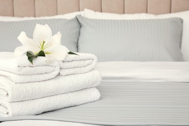 Photo of Stack of fresh towels with flower on bed indoors, space for text