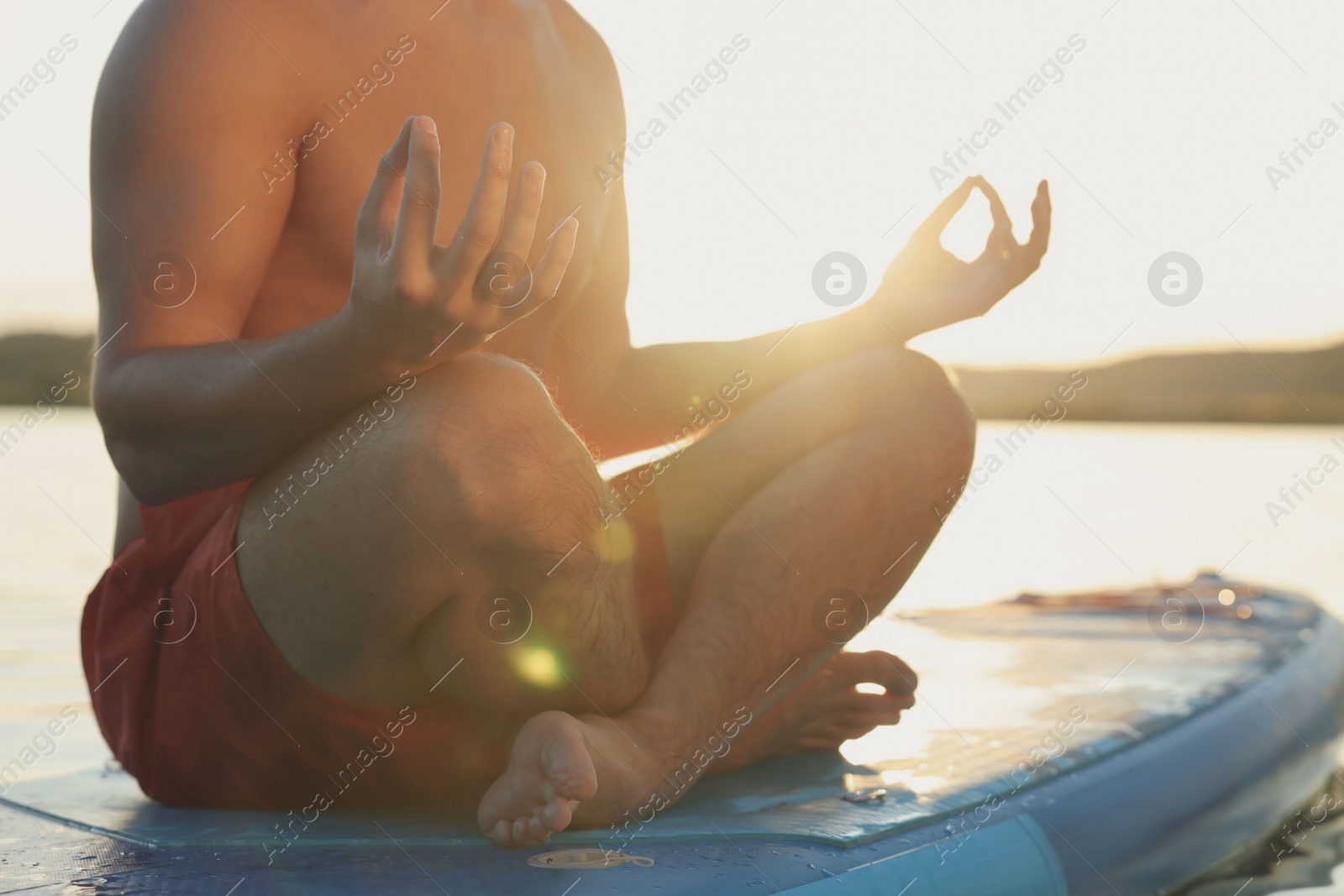 Photo of Man meditating on light blue SUP board on river at sunset, closeup