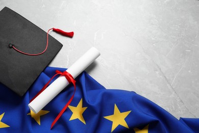 Photo of Black graduation cap, diploma and flag of European Union on light grey marble table, above view. Space for text