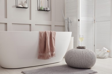 Photo of Stylish knitted pouf with glass of wine on floor in modern bathroom. Interior design