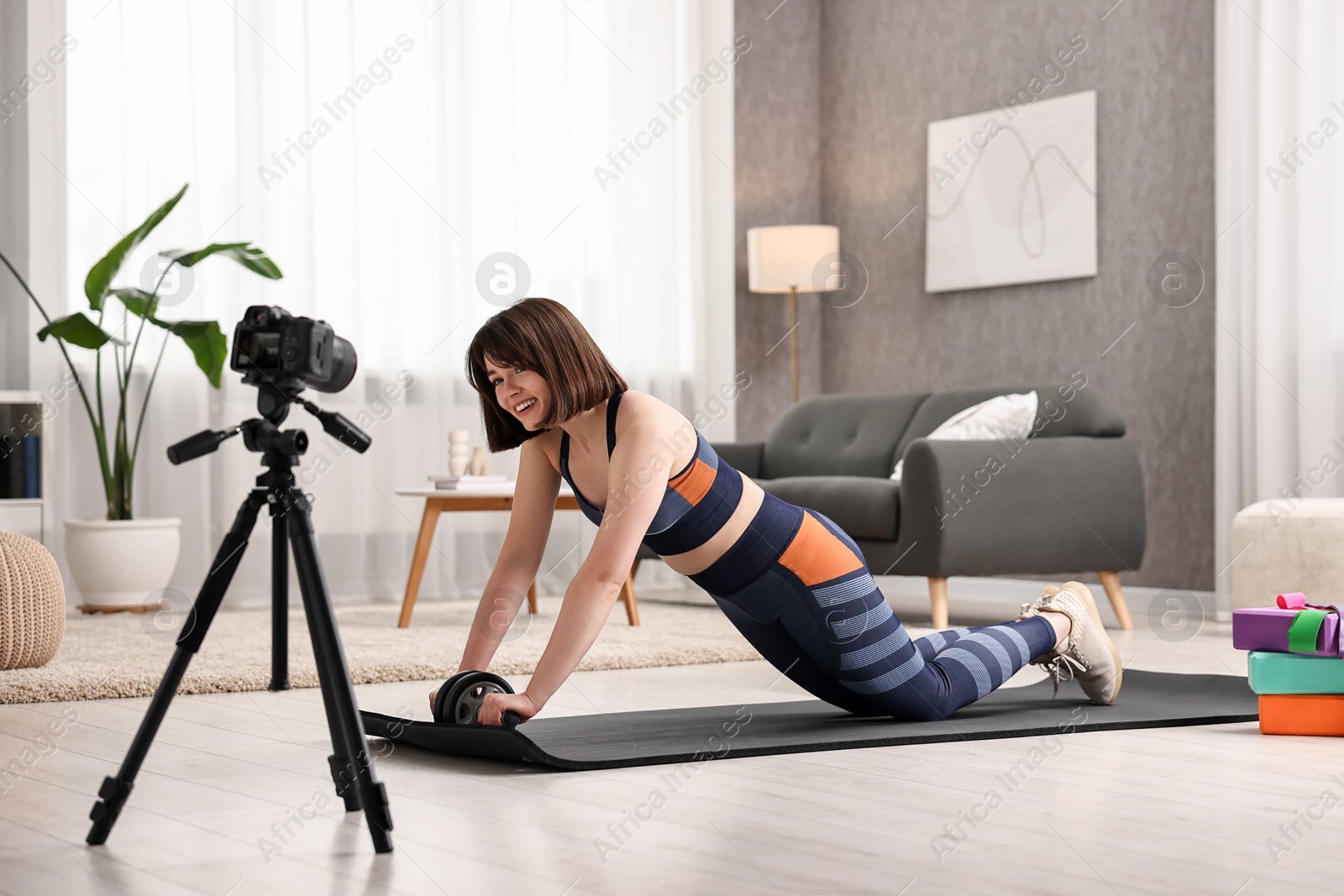 Photo of Happy sports blogger training with ab roller while recording fitness lesson at home