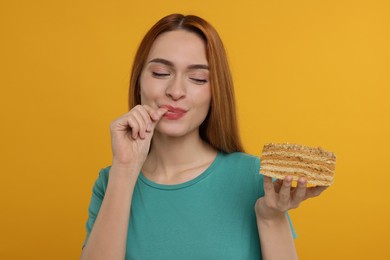 Young woman with piece of tasty cake on orange background