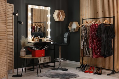 Makeup room. Stylish mirror near dressing table, chair and clothes rack indoors