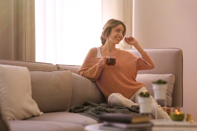 Photo of Beautiful young woman with cup of tea relaxing at home. Cozy atmosphere