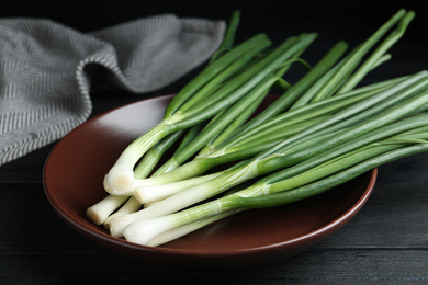 Photo of Fresh green spring onions on brown plate, closeup