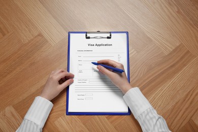 Woman filling visa application form for immigration at table, top view