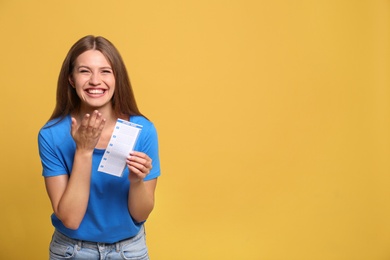 Photo of Portrait of happy young woman with lottery ticket on yellow background, space for text