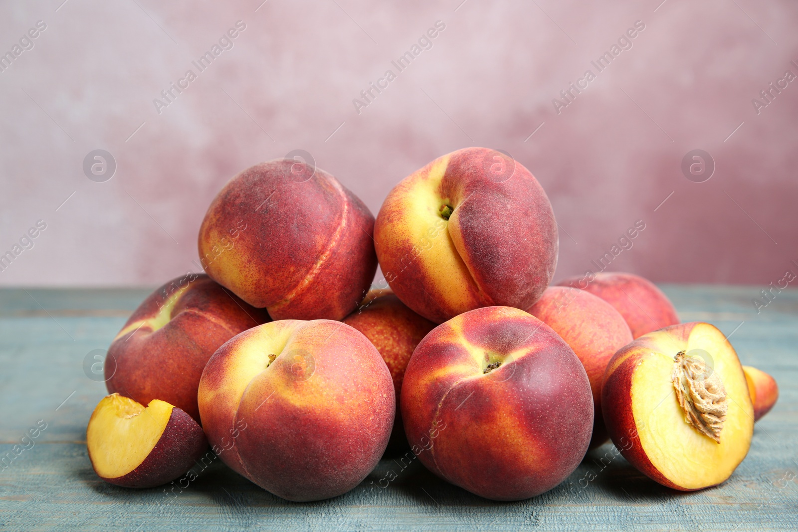 Photo of Pile of ripe peaches on blue wooden table against pink background