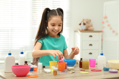 Photo of Cute little girl making DIY slime toy at table indoors