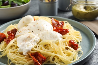 Photo of Delicious spaghetti with burrata cheese and sun dried tomatoes on grey table, closeup