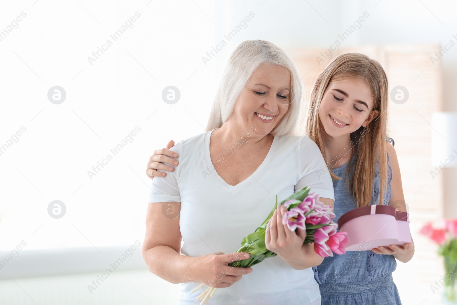 Photo of Happy mature woman receiving bouquet and gift from her teenage granddaughter at home