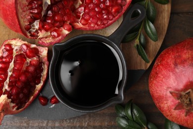 Photo of Tasty pomegranate sauce, fruits and branches on wooden table, flat lay