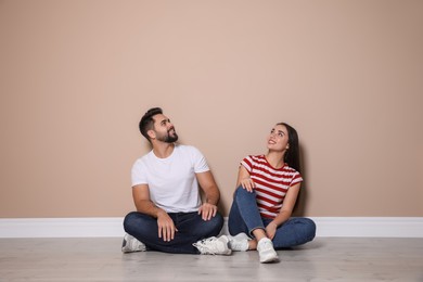 Photo of Young couple sitting on floor near beige wall indoors