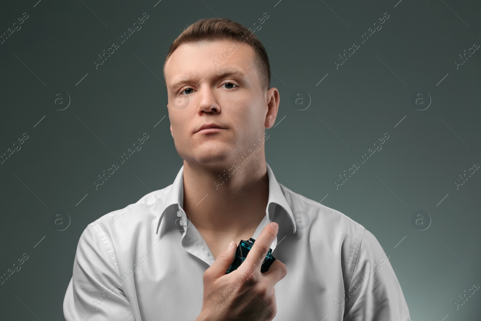 Photo of Handsome man in shirt using perfume on dark background