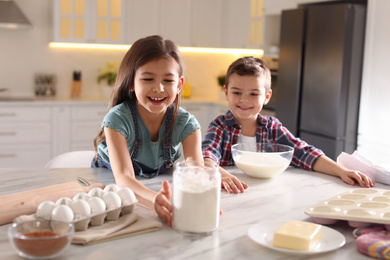 Photo of Cute little children cooking dough in kitchen at home