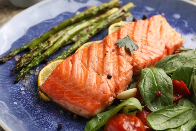 Photo of Tasty grilled salmon with tomatoes, asparagus, spinach and spices on plate, closeup