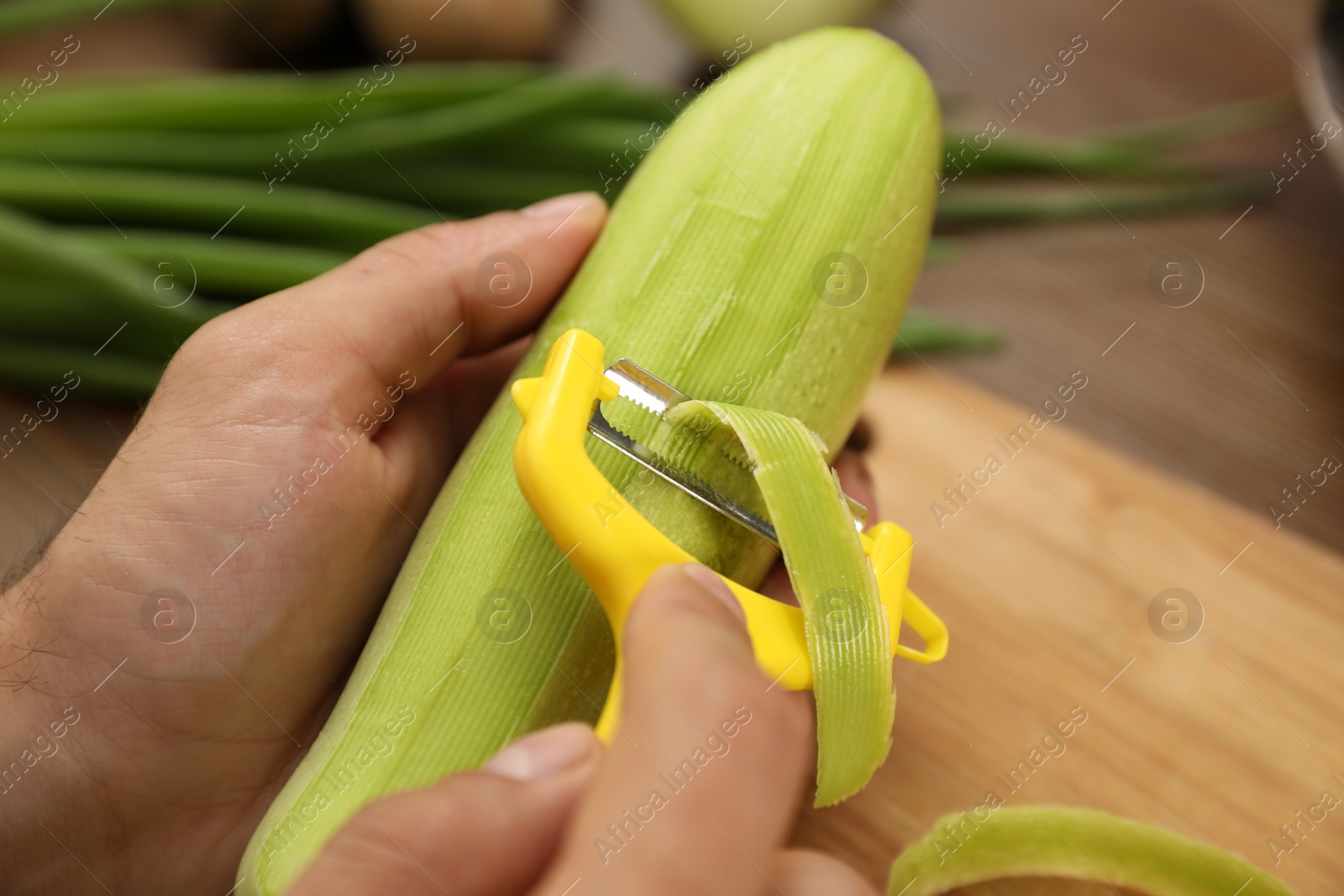 Photo of Man peeling zucchini at kitchen table, closeup. Preparing vegetable