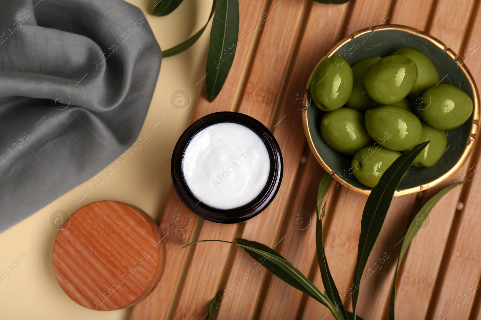 Photo of Jar of natural cream, olives and leaves on beige background, flat lay