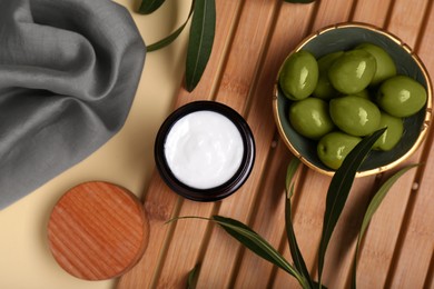 Jar of natural cream, olives and leaves on beige background, flat lay
