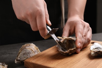 Photo of Man opening fresh oyster with knife at grey table, closeup