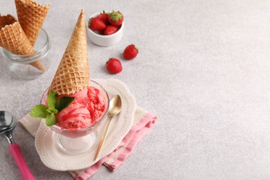 Photo of Delicious scoops of strawberry ice cream with mint and wafer cone in glass dessert bowl served on grey table. Space for text
