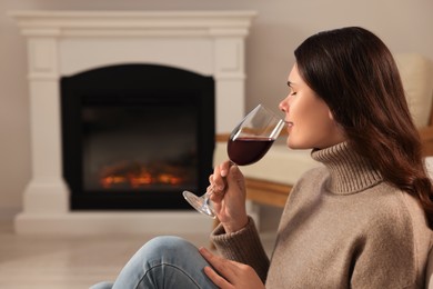 Photo of Young woman with glass of wine relaxing near fireplace at home. Space for text