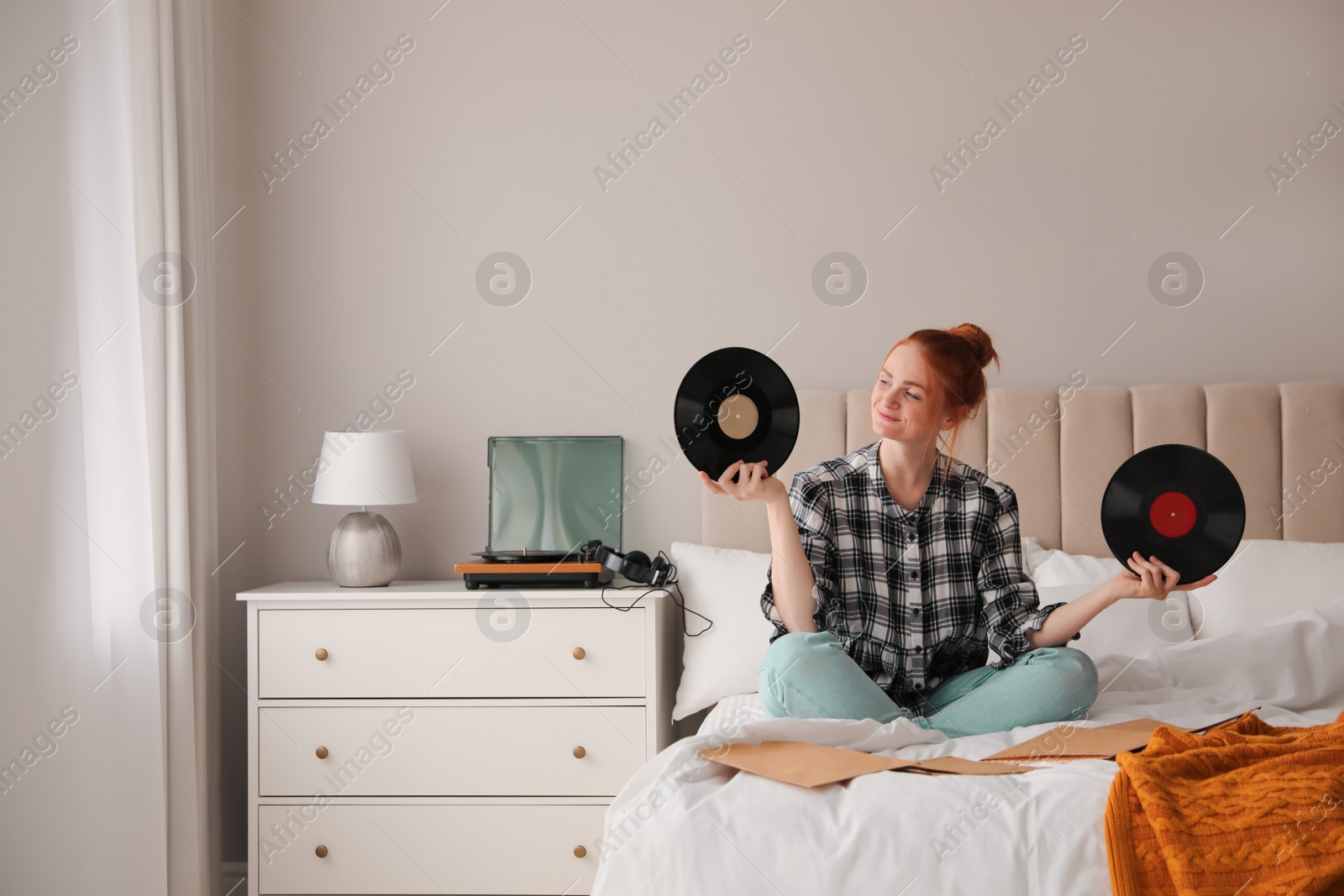 Photo of Young woman choosing vinyl disc to play music with turntable in bedroom