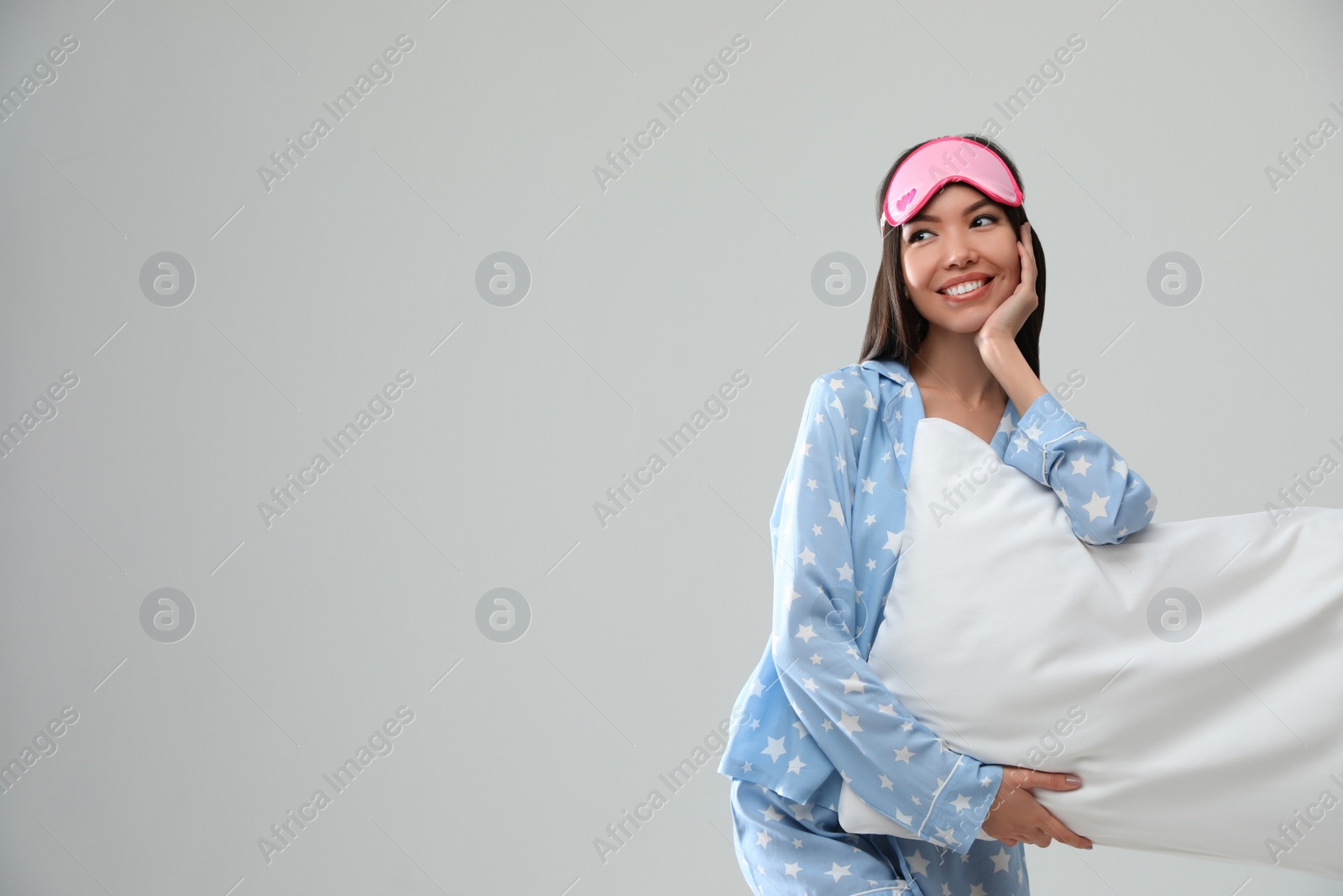 Photo of Beautiful Asian woman with pillow on light grey background, space for text. Bedtime