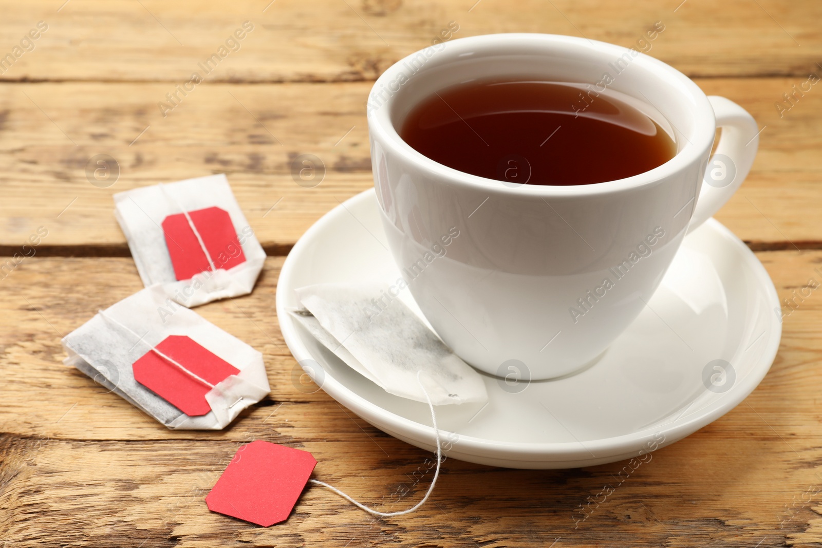 Photo of Tea bags and cup of hot beverage on wooden table, closeup