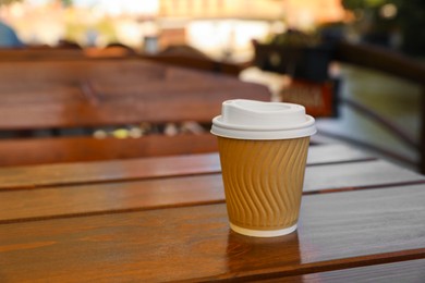 Photo of Takeaway paper cup with coffee on wooden table outdoors. Space for text