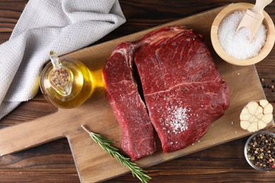 Photo of Fresh raw beef cuts with oil and spices on wooden table, top view