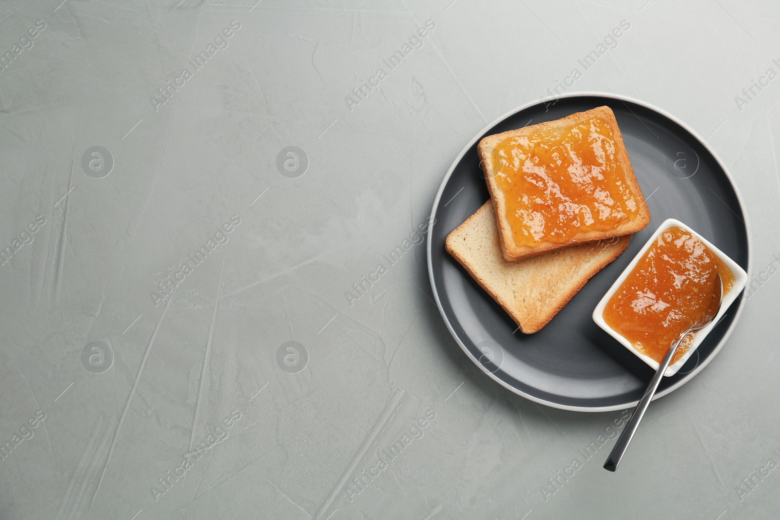 Photo of Toasts and orange jam on grey table, top view. Space for text