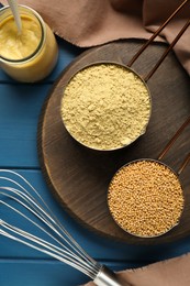 Photo of Saucepans with mustard powder and seeds on blue wooden table, flat lay