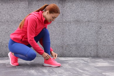Photo of Woman in gym clothes tying shoelace of sneakers on street, space for text
