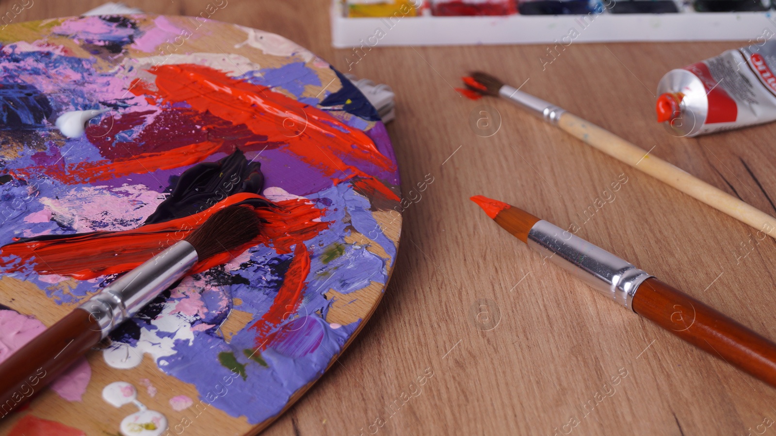 Photo of Artist's palette with mixed paints and brushes on wooden table