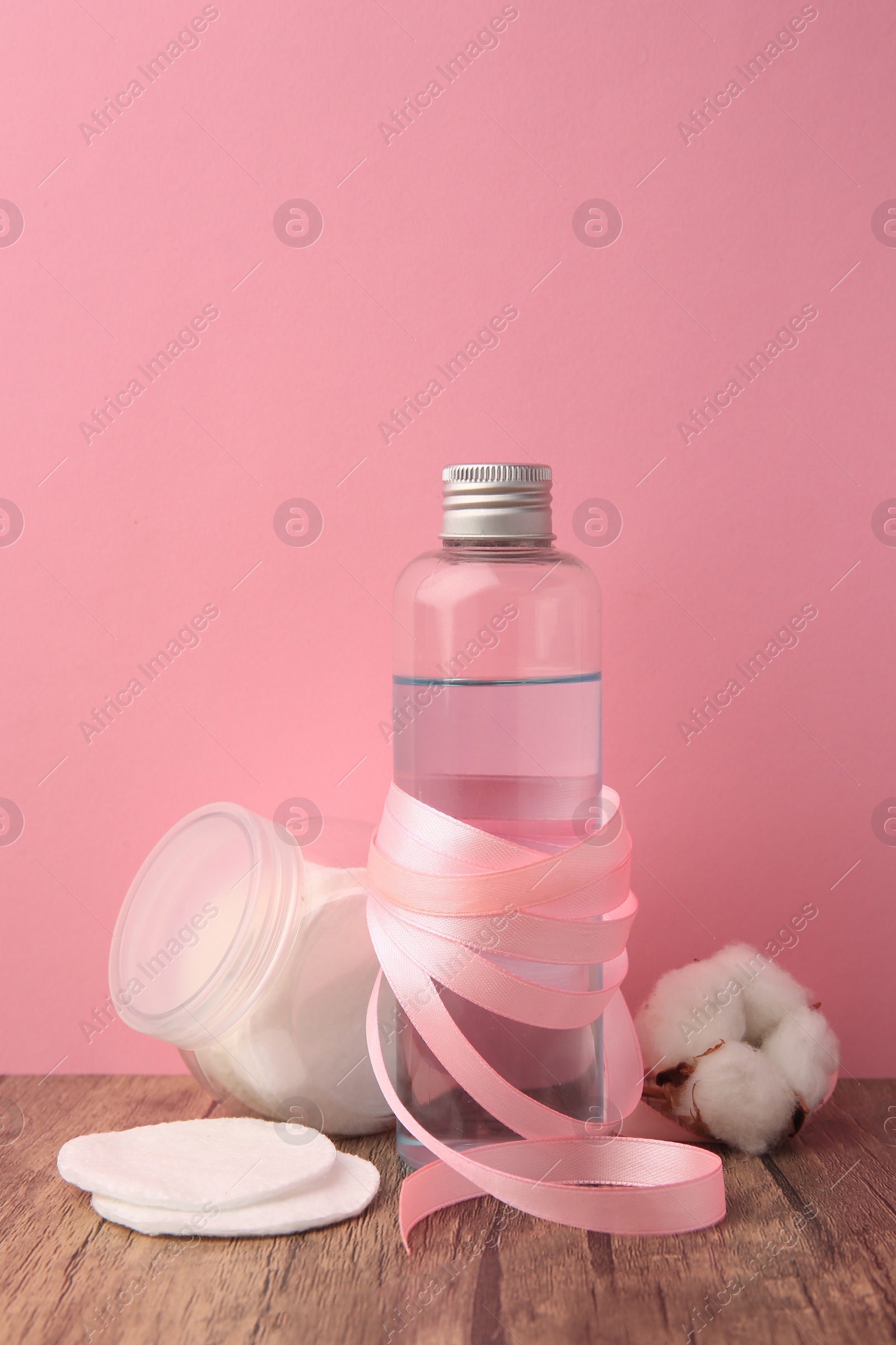 Photo of Composition with makeup remover and cotton flower on wooden table against pink background