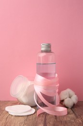 Photo of Composition with makeup remover and cotton flower on wooden table against pink background