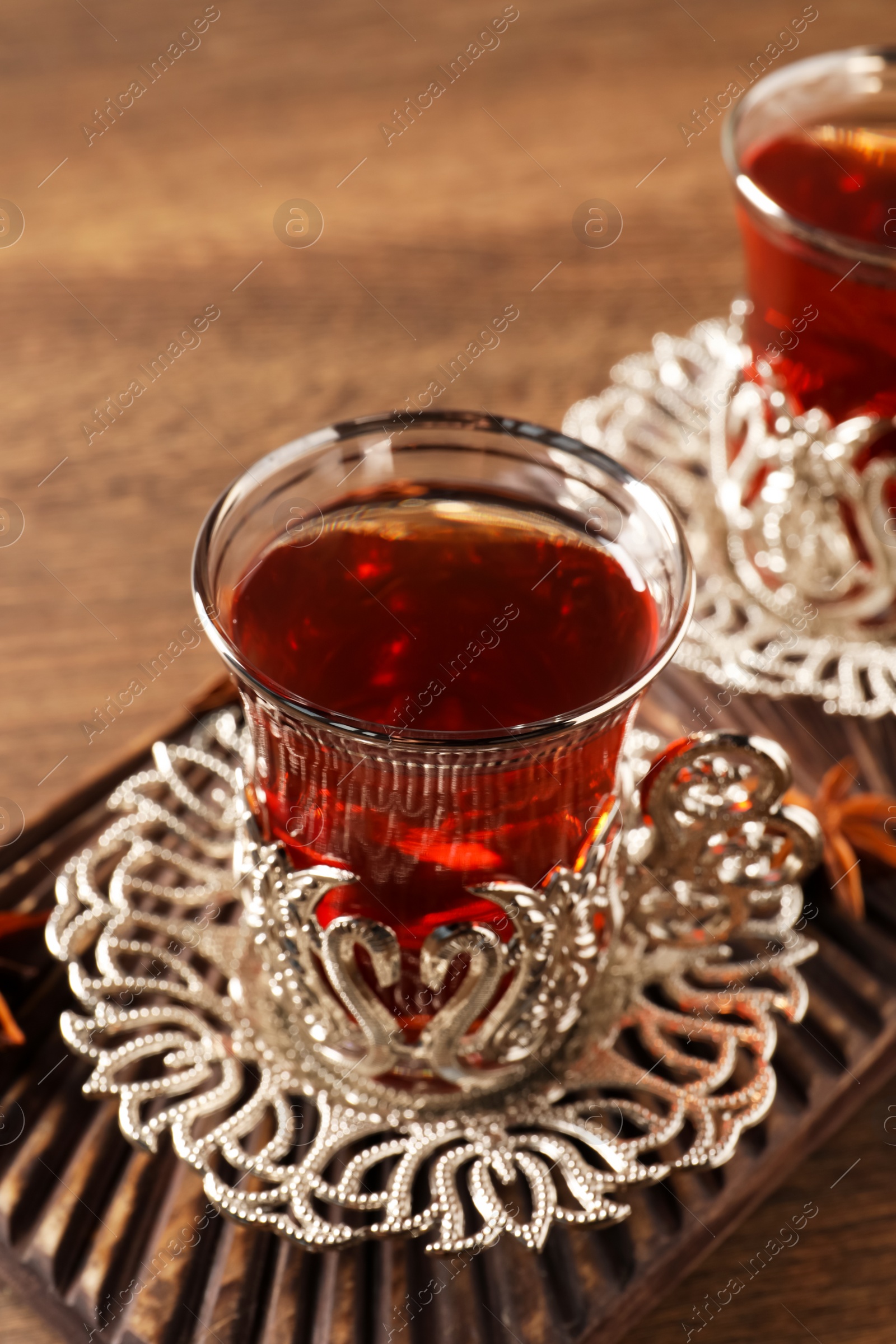 Photo of Glasses of traditional Turkish tea in vintage holders on wooden table, closeup