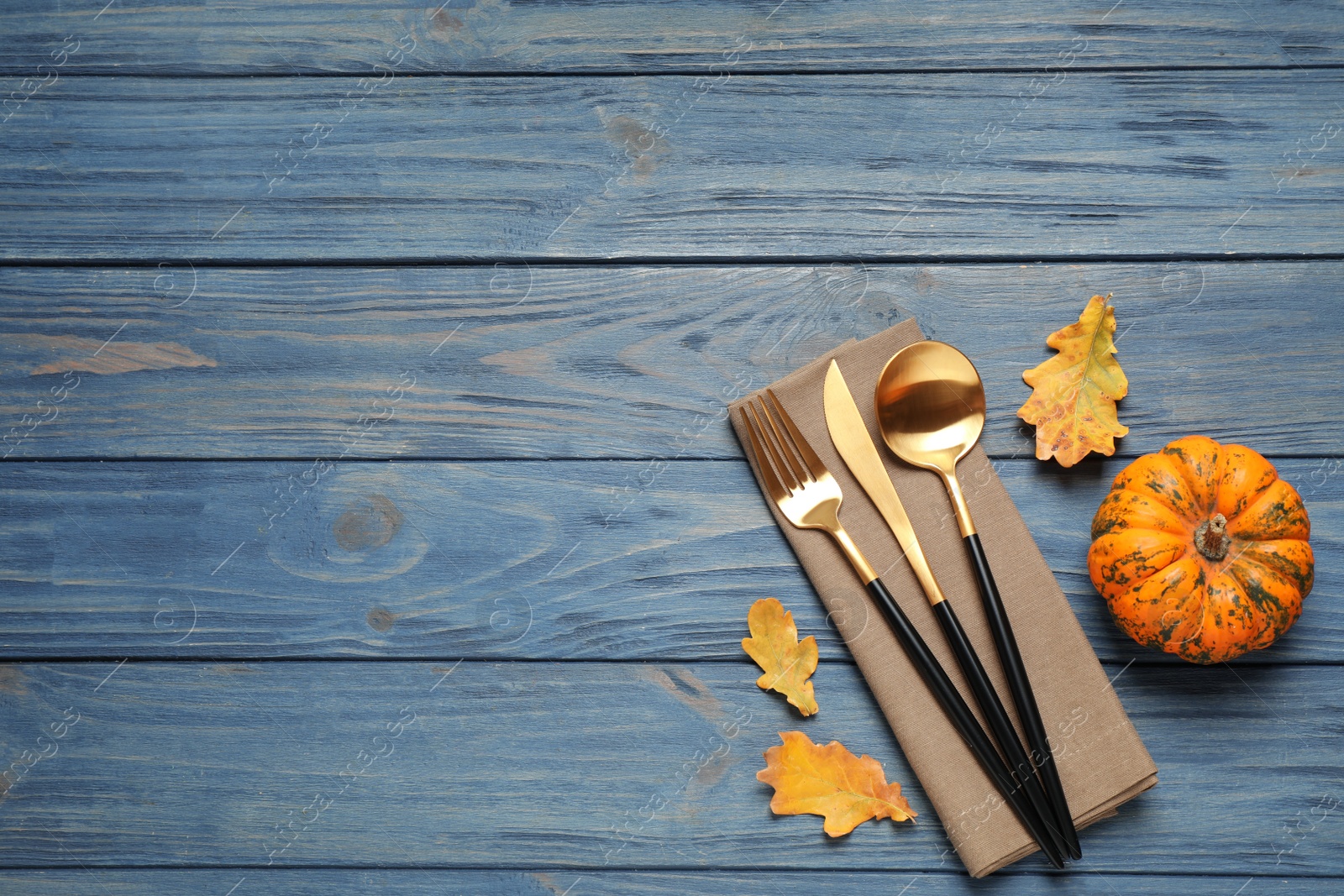 Photo of Cutlery, autumn leaves and pumpkin on blue wooden table, flat lay with space for text. Thanksgiving Day