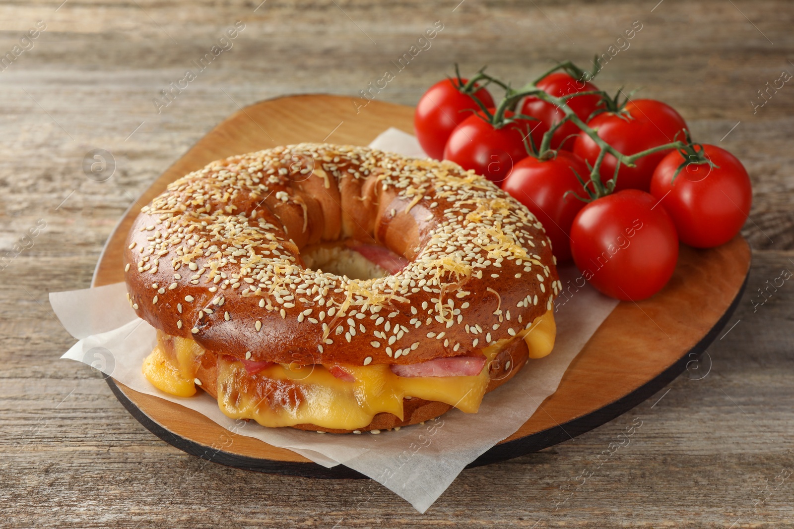 Photo of Delicious bagel with ham, cheese and tomatoes on wooden table