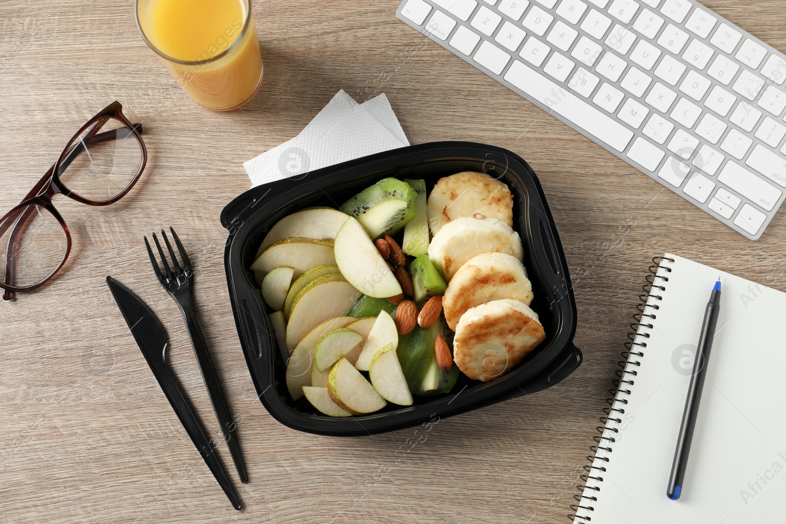 Photo of Container with tasty food, keyboard, cutlery and glasses on wooden table, flat lay. Business lunch