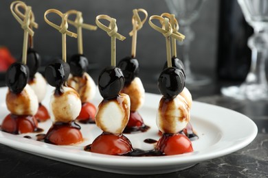 Photo of Tasty canapes with black olives, mozzarella and cherry tomatoes on dark textured table, closeup