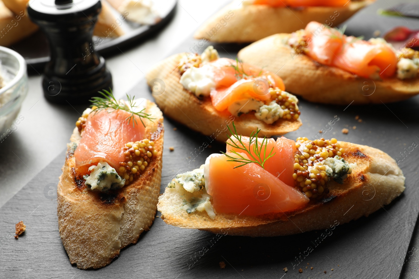 Photo of Tasty bruschettas with salmon and blue cheese on slate plate, closeup